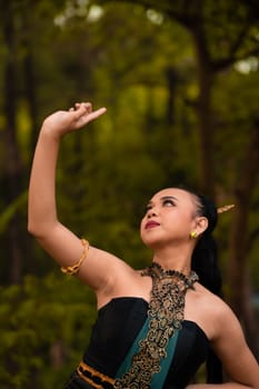 Balinese women raise their hands in the air while dancing in green costumes while performing in the festival in front of the jungle