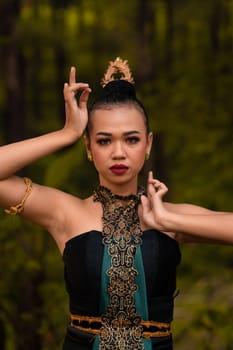 Brave Face of an Asian woman in a traditional green costume with golden accessories on her body during the competition in a dance festival in front of the forest