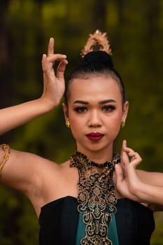 Brave Face of an Asian woman in a traditional green costume with golden accessories on her body during the competition in a dance festival in front of the forest