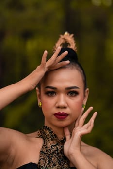 Brave Face of an Asian woman in a traditional green costume with golden accessories on her body during the competition in a dance festival in front of the forest