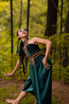 Beautiful Asian woman in a green costume with long black hair dances in the woods during the daylight