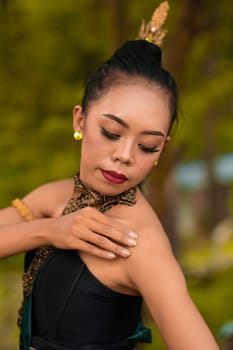 Portrait of a mystical woman in makeup with black hair and wearing a gold jewelry in front of the forest