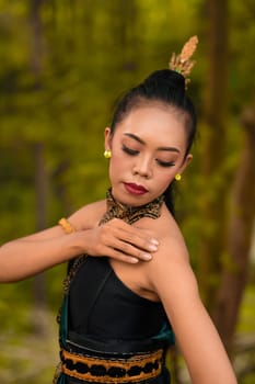 Portrait of a mystical woman in makeup with black hair and wearing a gold jewelry in front of the forest