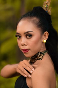 Portrait of a mystical woman in makeup with black hair and wearing a gold jewelry in front of the forest