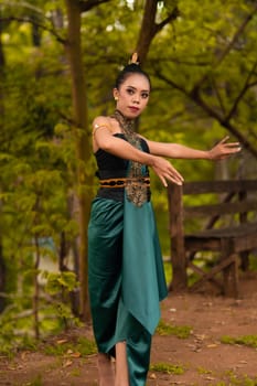 Javanese woman dancing in front of the woods in green costume while in makeup and performing at the village
