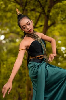Portrait of a beautiful Asian woman in makeup while dancing in front of the jungle with a black and green costume on her body during the daylight