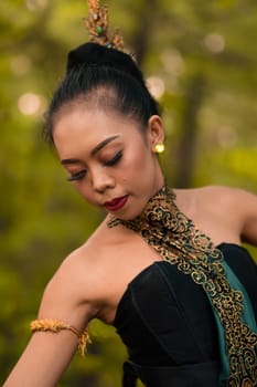 Portrait of a beautiful Asian woman in makeup while dancing in front of the jungle with a black and green costume on her body during the daylight