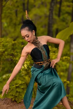 Indonesian woman dancing in the forest while wearing a traditional green costume during the festival inside the village