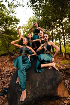 A Group of Asian people in green costumes sitting on a big rock with brown leaves in the background inside the forest