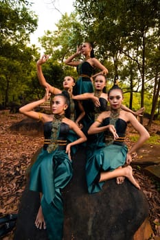 A Group of Asian people in green costumes sitting on a big rock with brown leaves in the background inside the forest