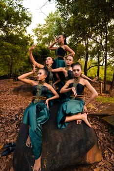 A Group of Asian people in green costumes sitting on a big rock with brown leaves in the background inside the forest
