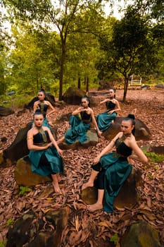 A Group of Indonesian dancers sitting gorgeously on the rock with brown leaves in the background inside the forest during the daylight
