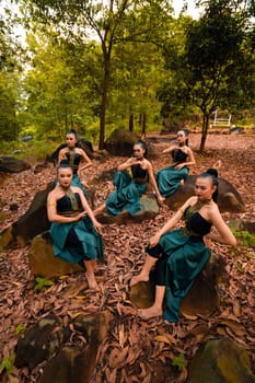 A Group of Indonesian dancers sitting gorgeously on the rock with brown leaves in the background inside the forest during the daylight