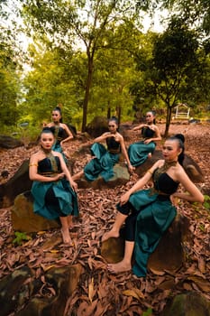 A Group of Indonesian dancers sitting gorgeously on the rock with brown leaves in the background inside the forest during the daylight