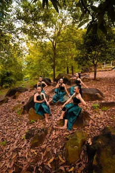 A Group of Indonesian dancers sitting gorgeously on the rock with brown leaves in the background inside the forest during the daylight