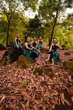 A Group of Asian women takes a vacation to the forest while wearing a green skirt and sitting on a rock during the morning