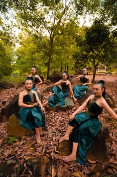 A Group of Indonesian dancers sitting gorgeously on the rock with brown leaves in the background inside the forest during the daylight