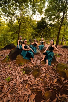 A Group of Asian women takes a vacation to the forest while wearing a green skirt and sitting on a rock during the morning