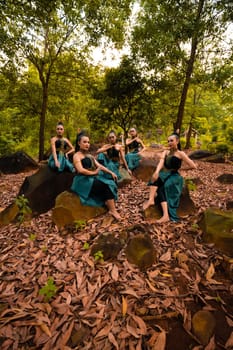 A Group of Asian women takes a vacation to the forest while wearing a green skirt and sitting on a rock during the morning