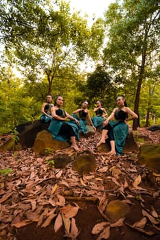 A Group of Asian women takes a vacation to the forest while wearing a green skirt and sitting on a rock during the morning