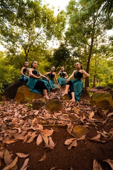A Group of Asian women takes a vacation to the forest while wearing a green skirt and sitting on a rock during the morning