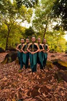A Beautiful Asian woman in a green costume standing together in front of the forest with brown leaves in the background