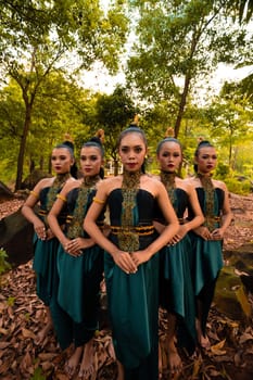 Glamor Asian women with green costumes and makeup line up together in the jungle with brown leaves on the ground