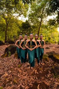 A Beautiful Asian woman in a green costume standing together in front of the forest with brown leaves in the background