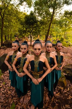 Glamor Asian women with green costumes and makeup line up together in the jungle with brown leaves on the ground