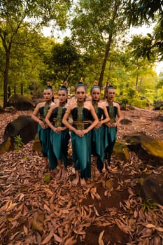a wide shot of an Asian woman standing together in the forest while wearing a green dance costume with dead leaves in the background