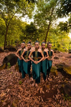 a wide shot of an Asian woman standing together in the forest while wearing a green dance costume with dead leaves in the background