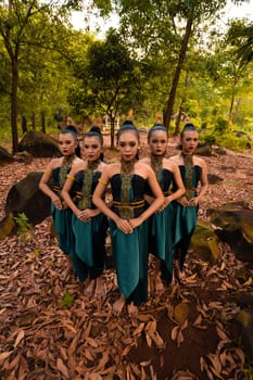 Glamor Asian women with green costumes and makeup line up together in the jungle with brown leaves on the ground