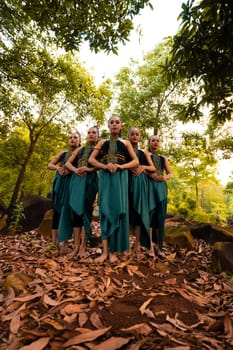 a wide shot of an Asian woman standing together in the forest while wearing a green dance costume with dead leaves in the background