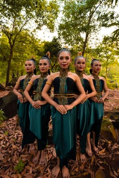 Glamor Asian women with green costumes and makeup line up together in the jungle with brown leaves on the ground