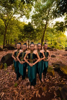 a wide shot of an Asian woman standing together in the forest while wearing a green dance costume with dead leaves in the background
