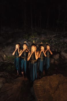 A Group of Indonesian women holding and wearing a brown wooden mask in a green skirt between the rock inside the woods