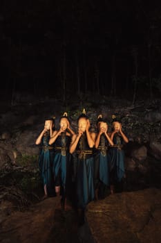 A Group of Indonesian women holding and wearing a brown wooden mask in a green skirt between the rock inside the woods