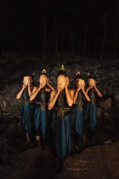 A Group of Indonesian women holding and wearing a brown wooden mask in a green skirt between the rock inside the woods