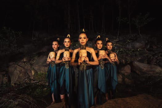 A Group of ethnical women holding a wooden craft mask in their hands while in line inside the wood in the night