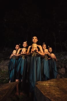 A Bunch of girls in green costumes holding a wooden masks in their hands while standing between the big rocks in front of the forest