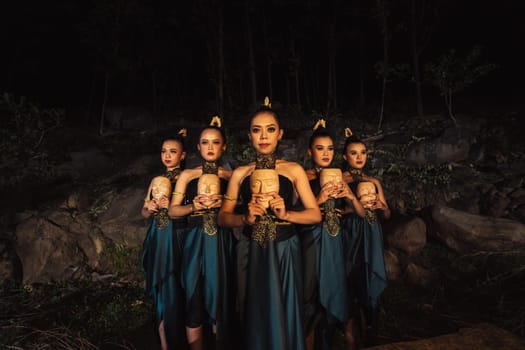 A Group of ethnical women holding a wooden craft mask in their hands while in line inside the wood in the night