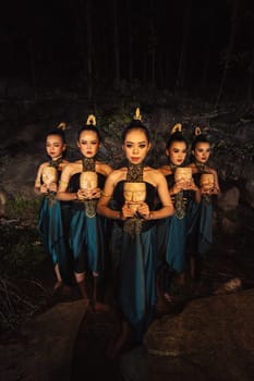 A Group of ethnical women holding a wooden craft mask in their hands while in line inside the wood in the night