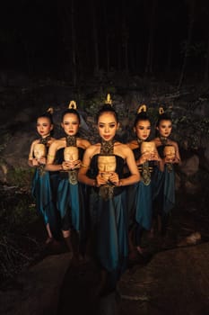 A Group of ethnical women holding a wooden craft mask in their hands while in line inside the wood in the night