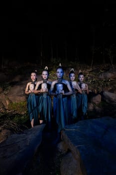 A Group of Javanese women standing in the woods between the rocks while holding a wooden mask inside the village