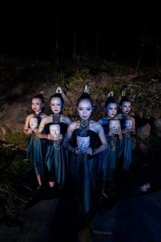 A Group of Balinese woman line up with the wooden mask in their hands while wearing a traditional dance costumes in the night