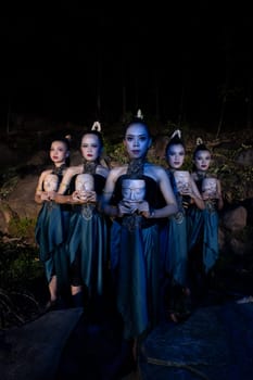 A Group of Javanese women standing in the woods between the rocks while holding a wooden mask inside the village
