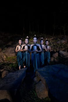 A Group of Javanese women standing in the woods between the rocks while holding a wooden mask inside the village