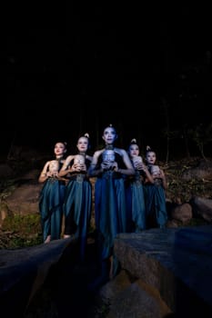 A Group of Javanese women standing in the woods between the rocks while holding a wooden mask inside the village