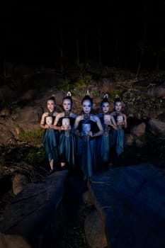 A Group of Javanese women standing in the woods between the rocks while holding a wooden mask inside the village