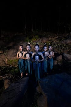 A Group of Javanese women standing in the woods between the rocks while holding a wooden mask inside the village